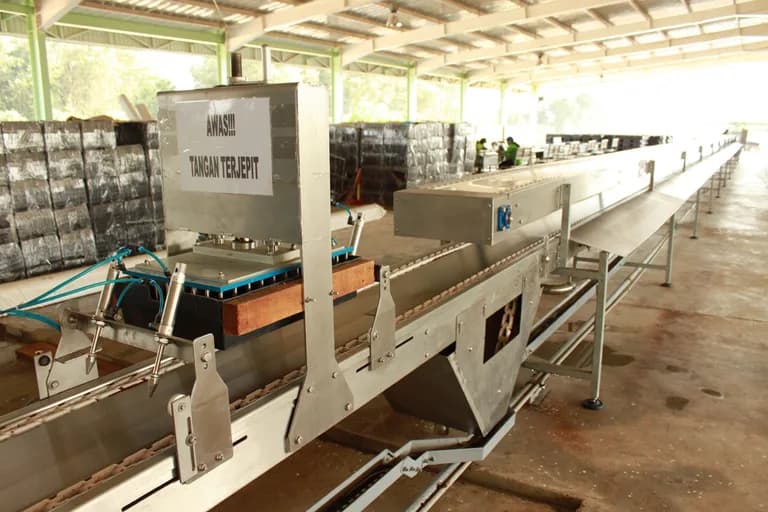 Stainless-steel conveyor and press line with safety signage and stacked growing-media bags.