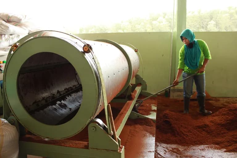 Rotary drum sieve machine discharging soil-based growing media, with a worker raking the pile.